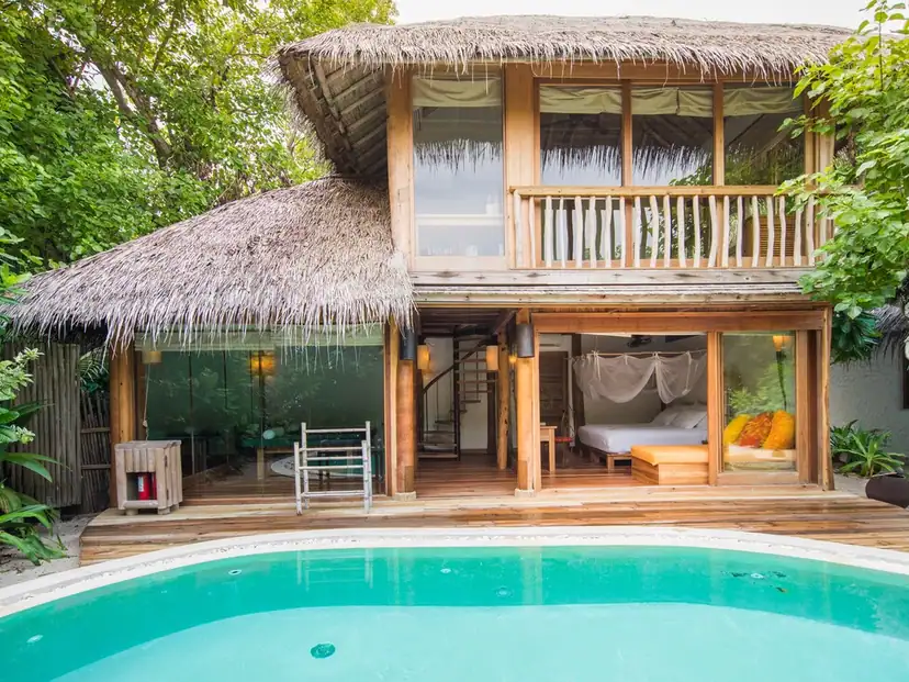 صورة: Soneva Fushi: A thatched two-story villa opens onto a wooden deck and pool, surrounded by tropical greenery.