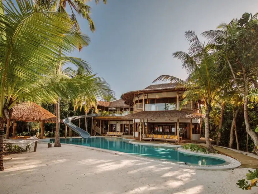صورة: Soneva Fushi: A spacious tropical villa opens onto a private pool with a waterslide, surrounded by palms and sandy grounds.