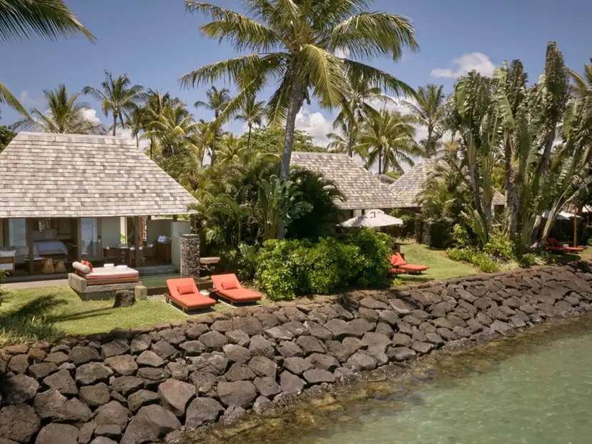 صورة: Four Seasons Resort Mauritius at Anahita: Tropical villas open onto a palm-lined shoreline, with orange sun loungers on the lawn beside the water.