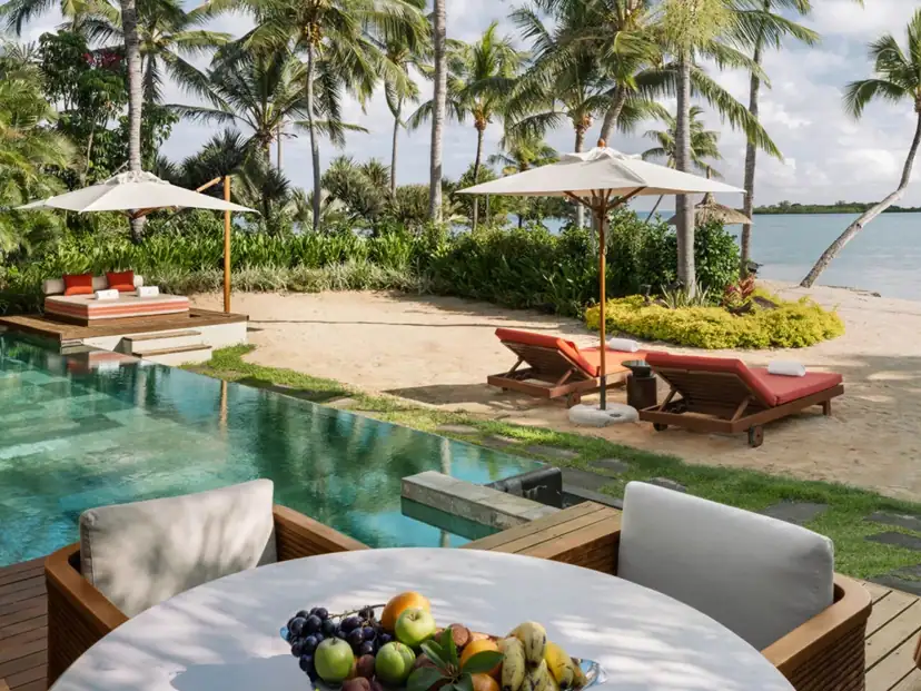 صورة: Four Seasons Resort Mauritius at Anahita: A poolside terrace with shaded loungers and outdoor seating sits beside a sandy beach lined with palms.