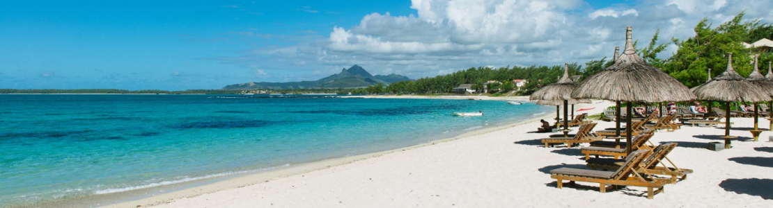Relax on the sandy beach beside turquoise water, with sun loungers and thatched umbrellas.