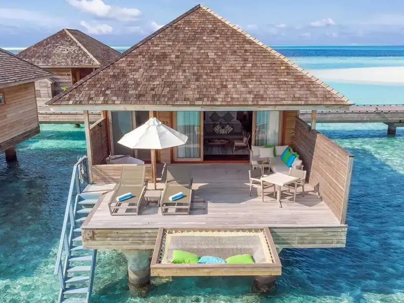 صورة: Hurawalhi Island Resort: An overwater villa with a spacious wooden deck, sun loungers, outdoor seating, and a netted daybed above clear turquoise water.