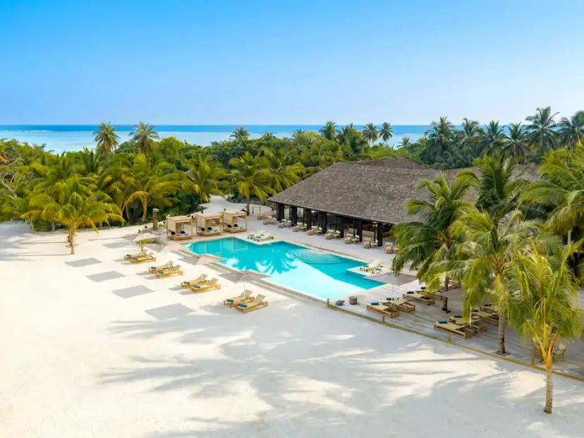 Nala Maldives by Jawakara: A turquoise resort pool with sun loungers and cabanas sits beside a palm-lined white-sand beach.