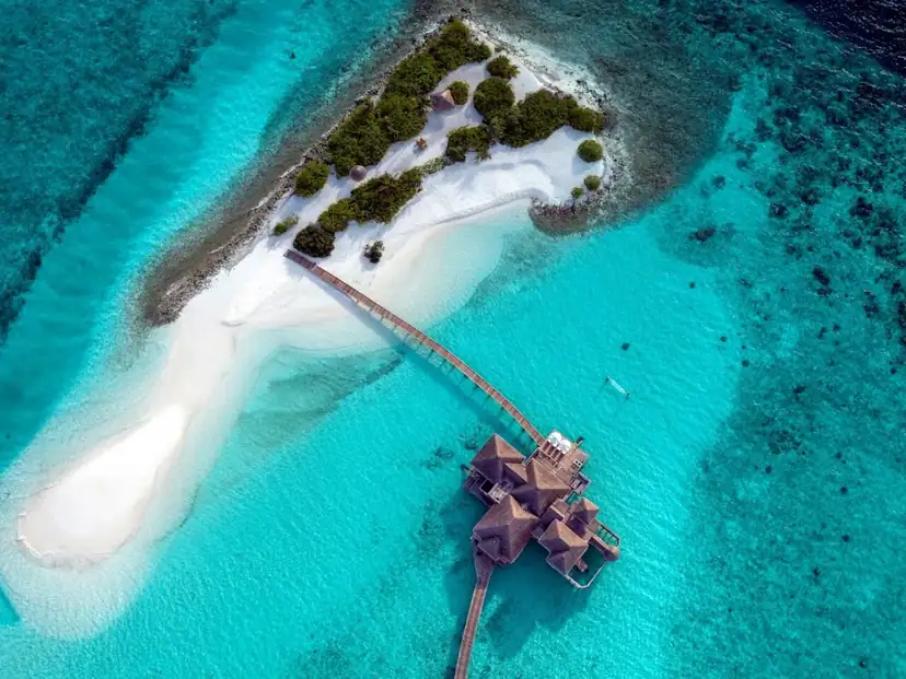 صورة: Gili Lankanfushi: A wooden walkway connects overwater villas to a lush island edged by white-sand beach and clear turquoise water.