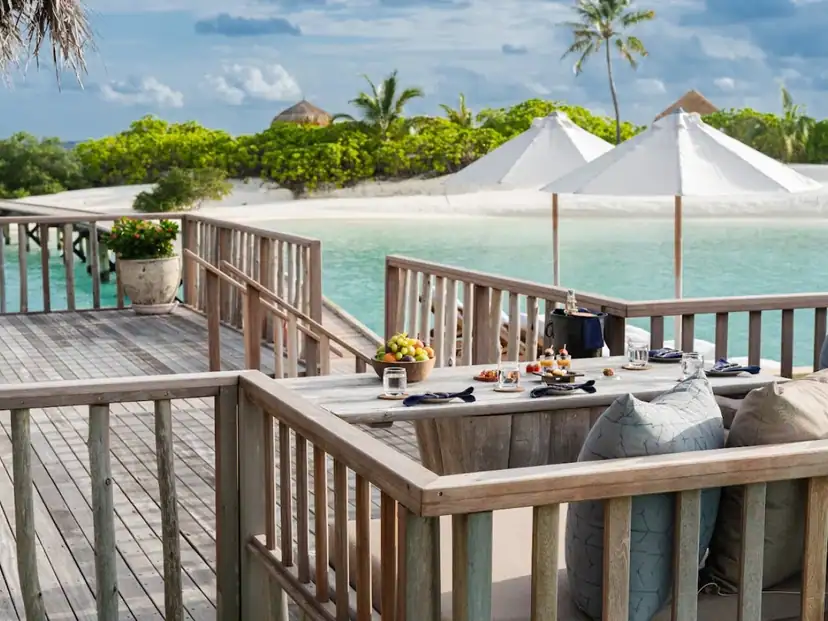 صورة: Gili Lankanfushi: Enjoy a table set for dining on a wooden terrace overlooking the turquoise lagoon and sandy beach.
