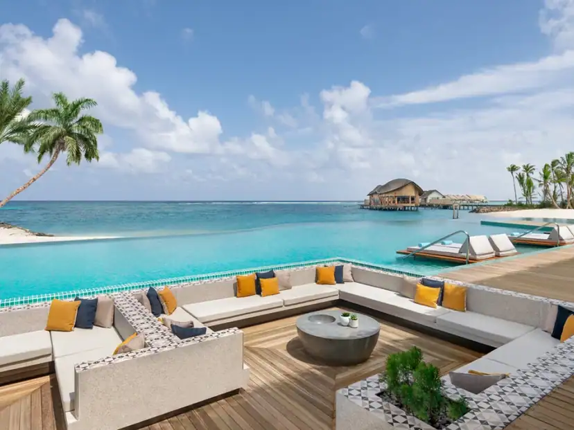 Hilton Maldives Amingiri Resort & Spa: An infinity pool overlooks the turquoise ocean, with sun loungers and a spacious outdoor lounge on the wooden deck.