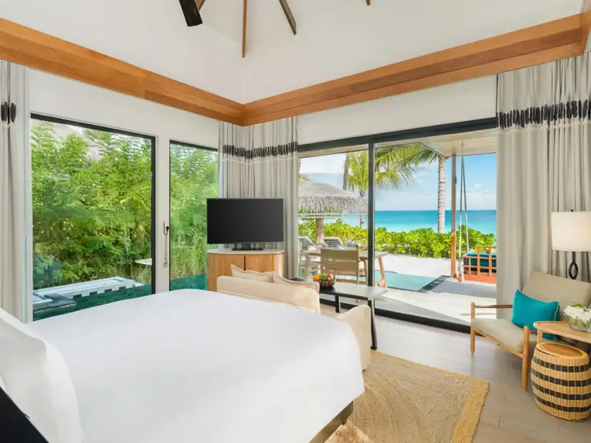 Hilton Maldives Amingiri Resort & Spa: Bright bedroom with a furnished patio, turquoise water, and ocean views.