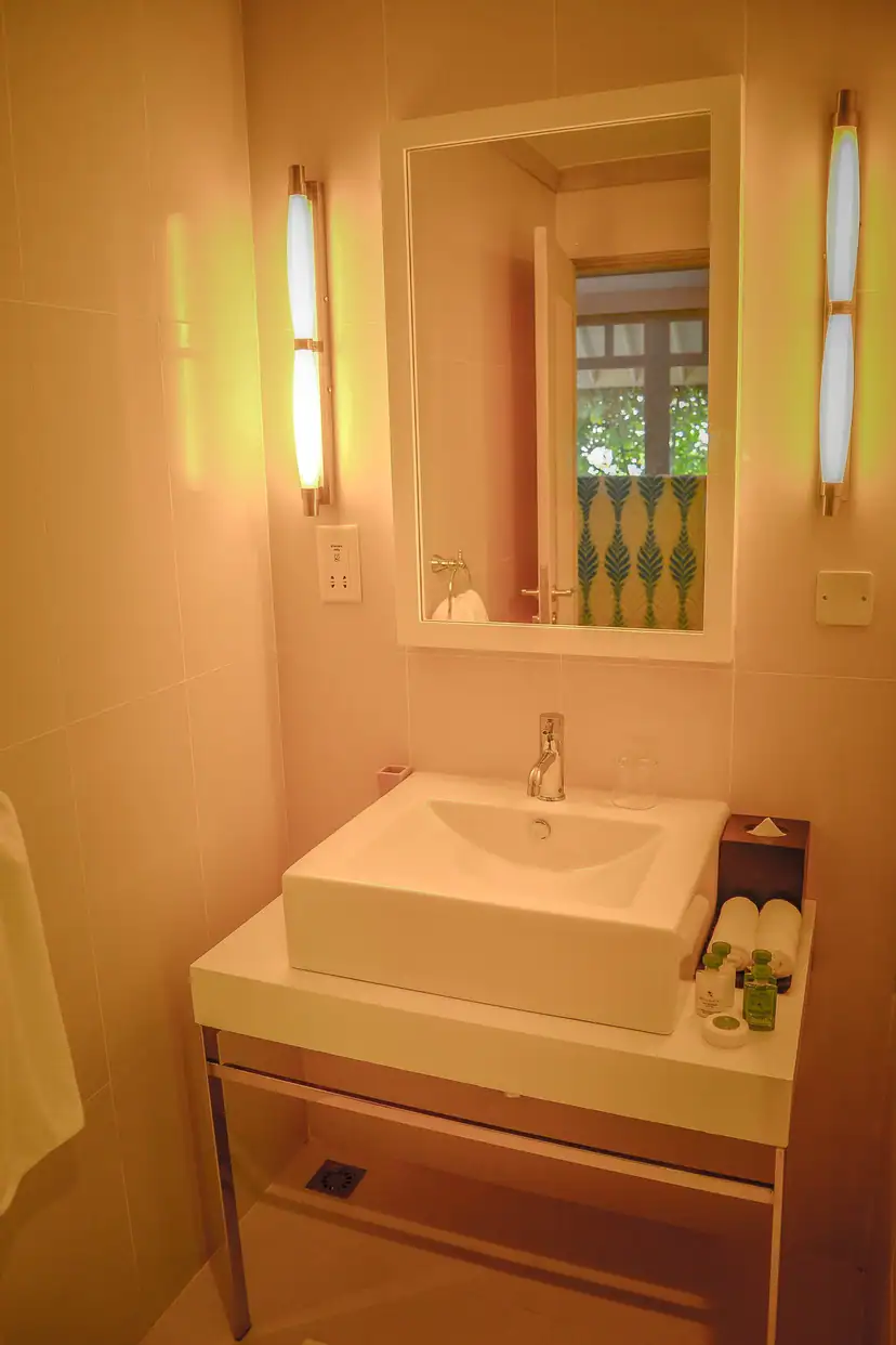 صورة: NH Maldives Kuda Rah Resort: A tiled bathroom vanity features a white basin, large mirror, toiletries, and slippers.