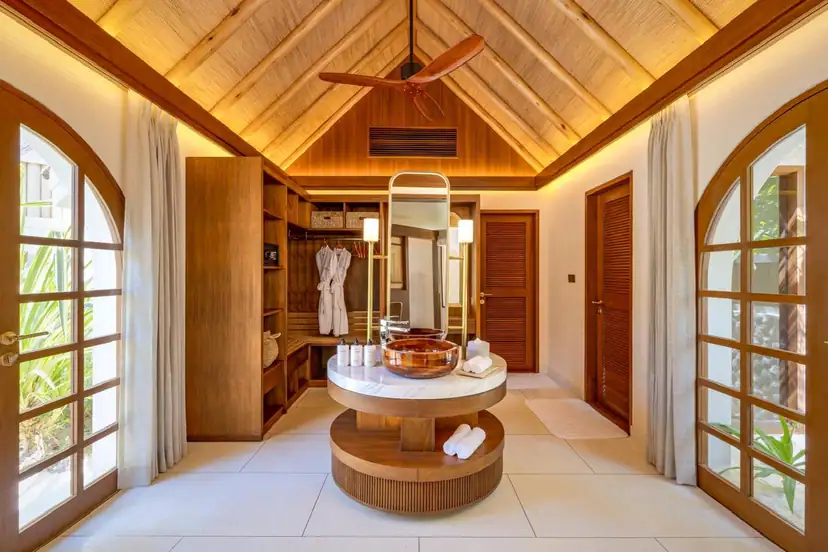 صورة: Rah Gili Maldives: Spacious bathroom featuring a central marble vanity with a copper sink, vaulted thatched ceiling, and arched glass doors opening to tropical gardens.